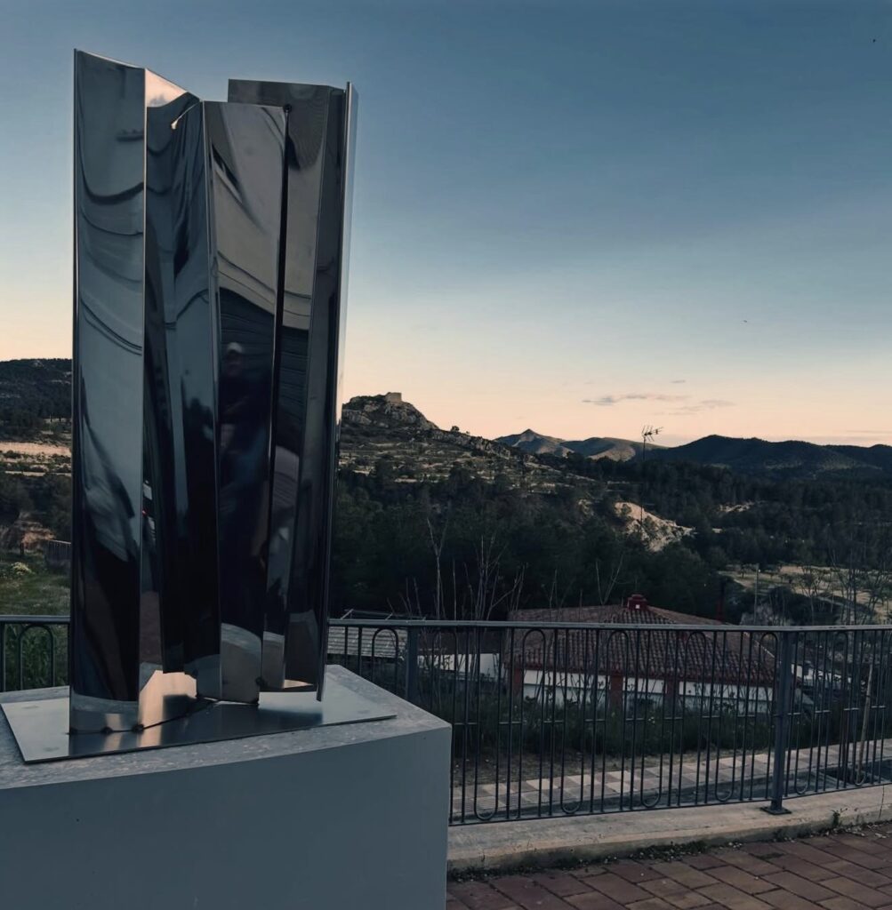 Escultura de acero reflectante de Eduardo Lastres en el Mirador del carrer Els Llorers, Tibi, con la sierra al fondo