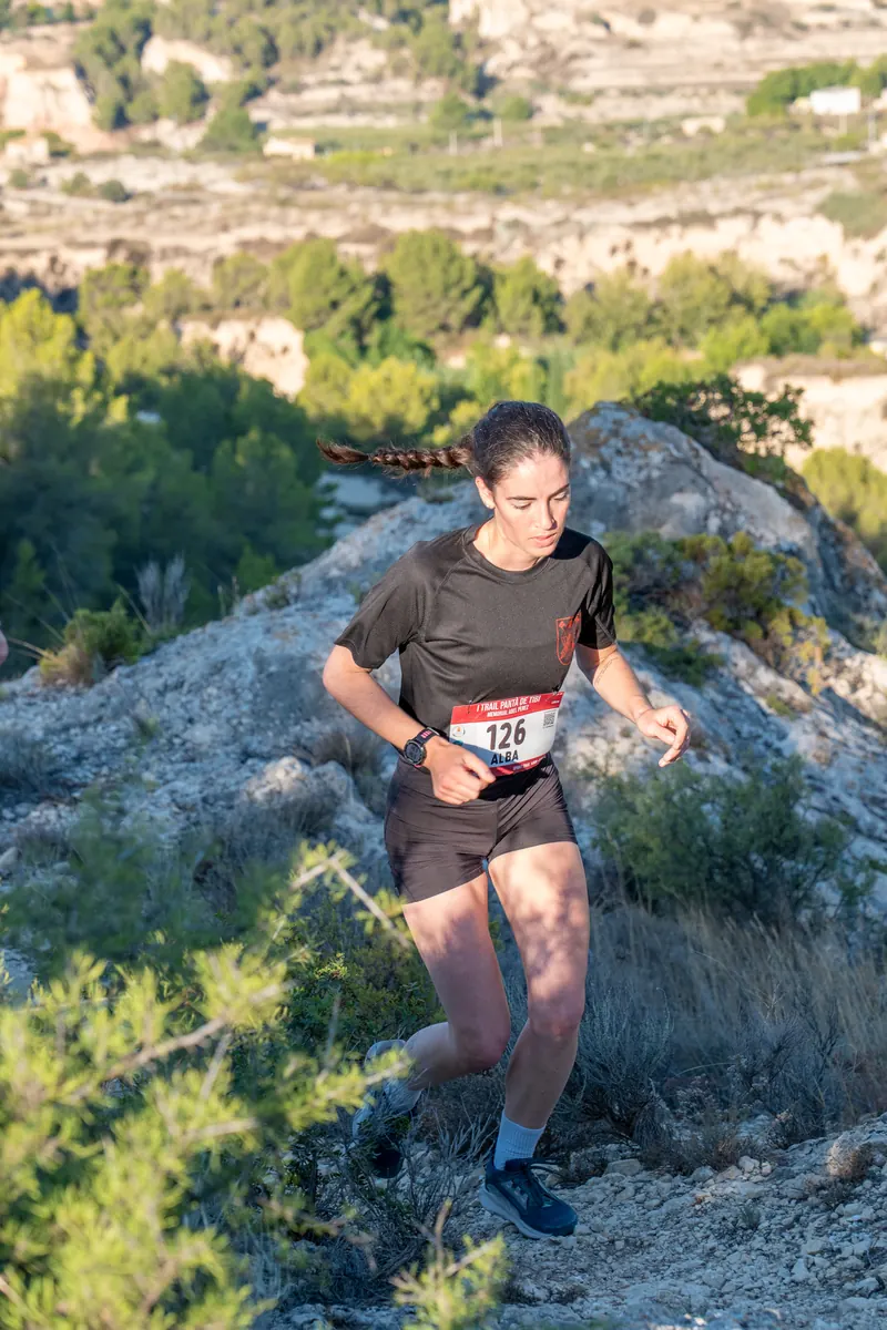 Corredora subiendo por una senda rocosa con el valle de Tibi al fondo